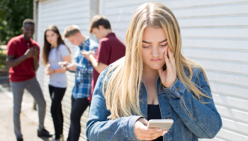 A girl gazes at her phone, standing before a group of people